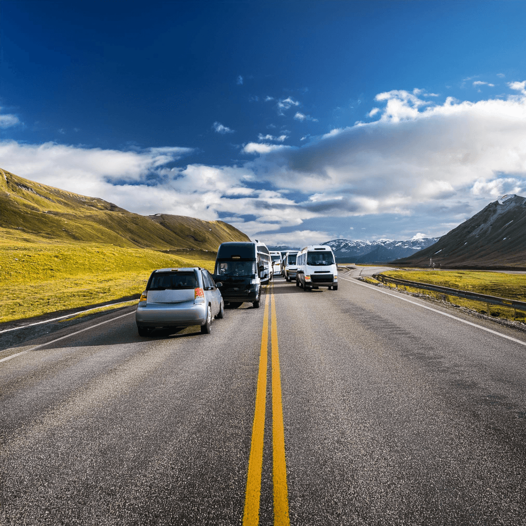 Cars and vans driving along an open road in a mountainous landscape under a partly cloudy blue sky.